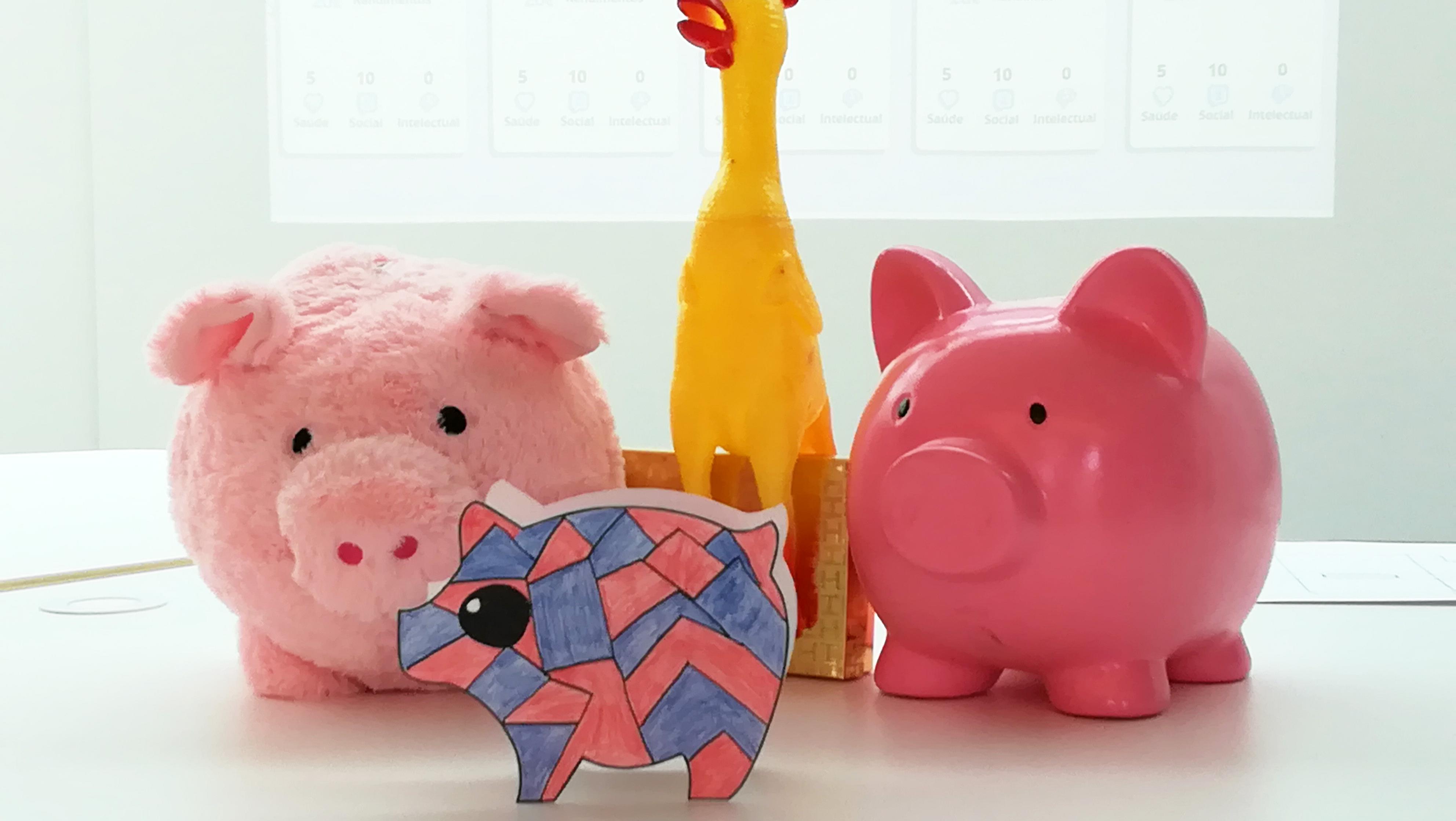 Três porquinhos mealheiros. Um de peluche, um de loiça e um de papel. Acompanhados de uma galinha de plástico.