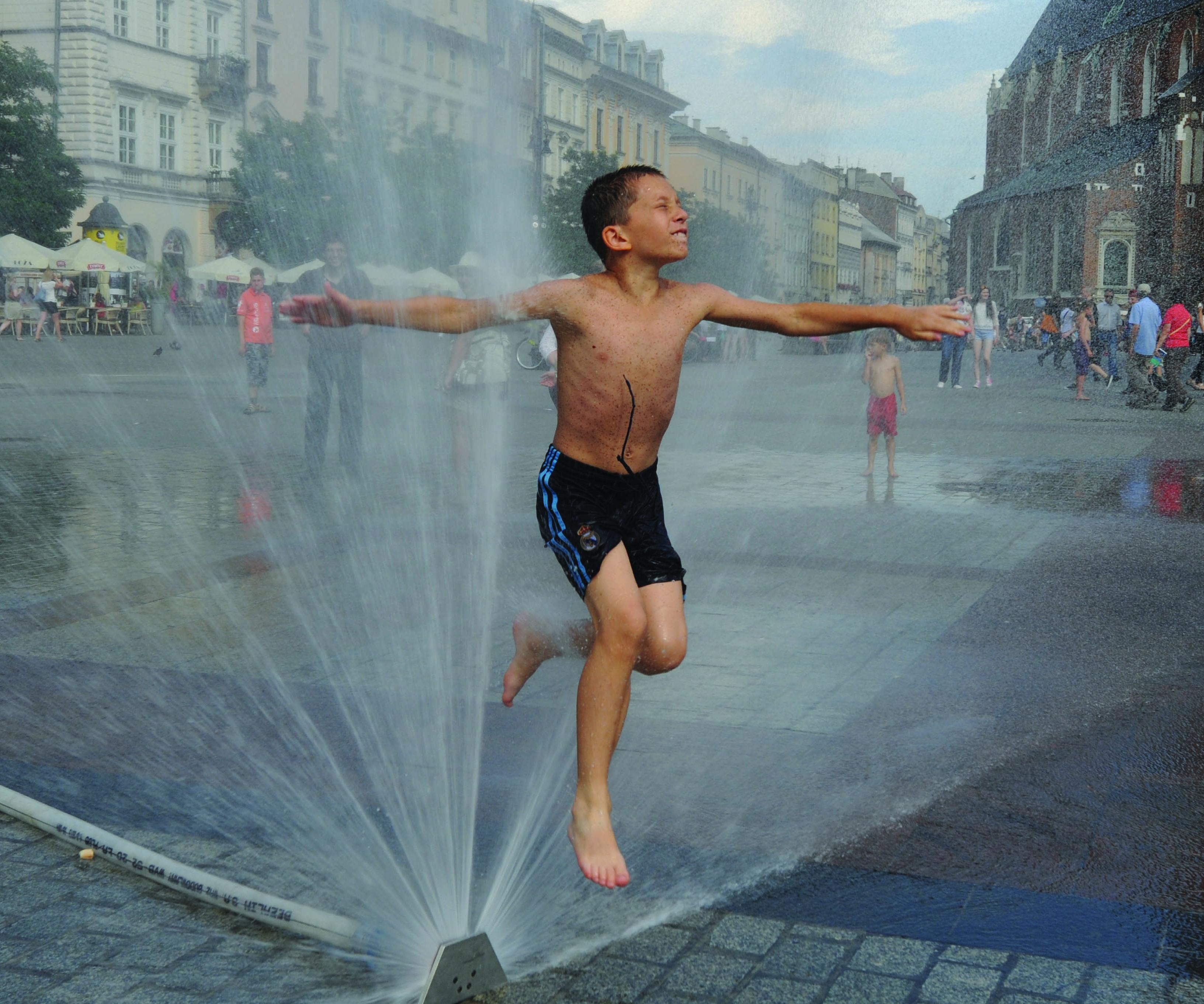 Fotografia na rua de criança em calções de banho a saltar por cima de repuxo