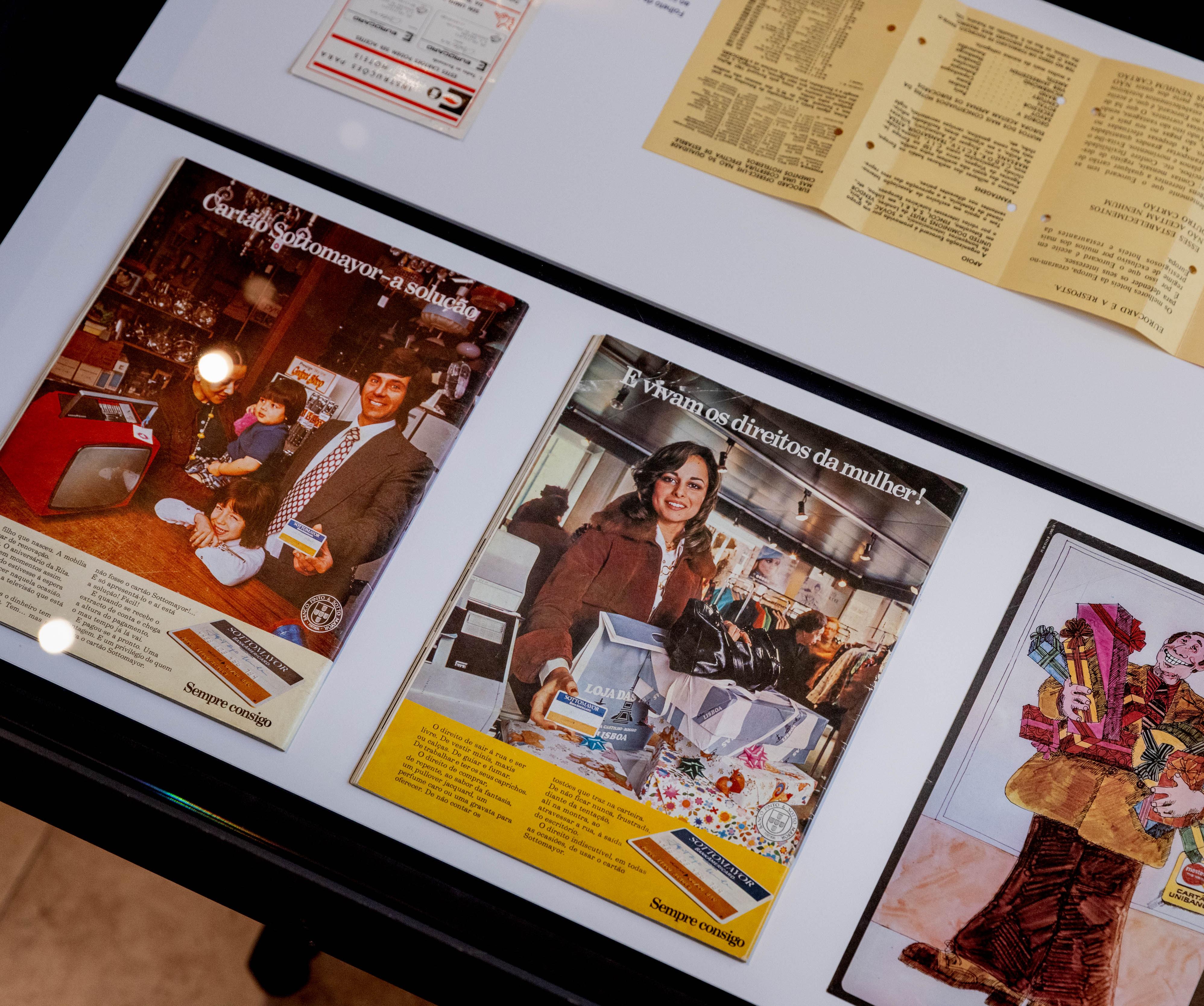 Fotografia do interior de vitrine com materiais publicitários (revistas) na exposição "Dinheiro de Plástico: a incrível história dos cartões bancários"
